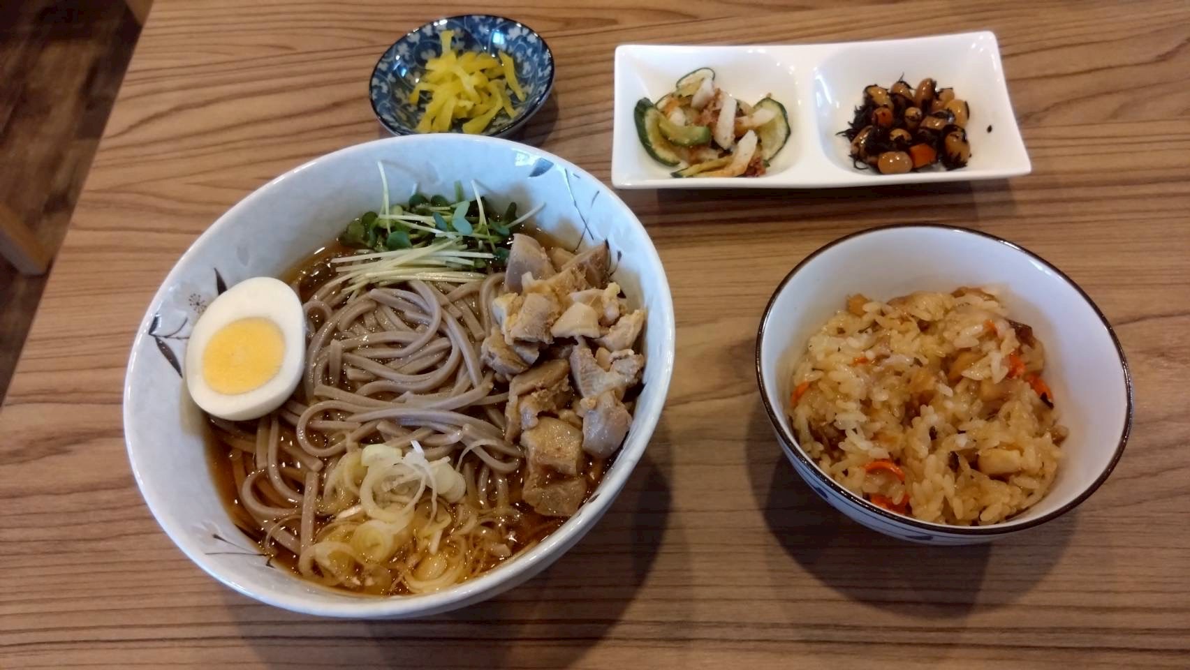 山形の肉そばとおこわ、小鉢が並ぶセット。肉そばは親鳥の肉と薬味がのり、別皿で漬物と小鉢が添えられている