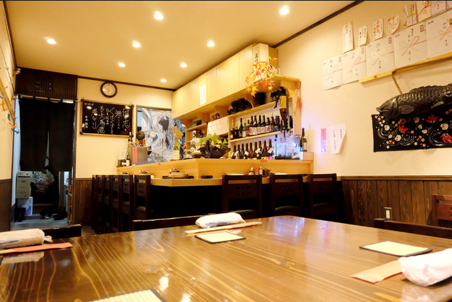 和洋創作居酒屋丸の店内。木目のテーブル席とカウンター席が並び、温かい照明の下で落ち着いて食事ができる雰囲気が伝わる店内写真