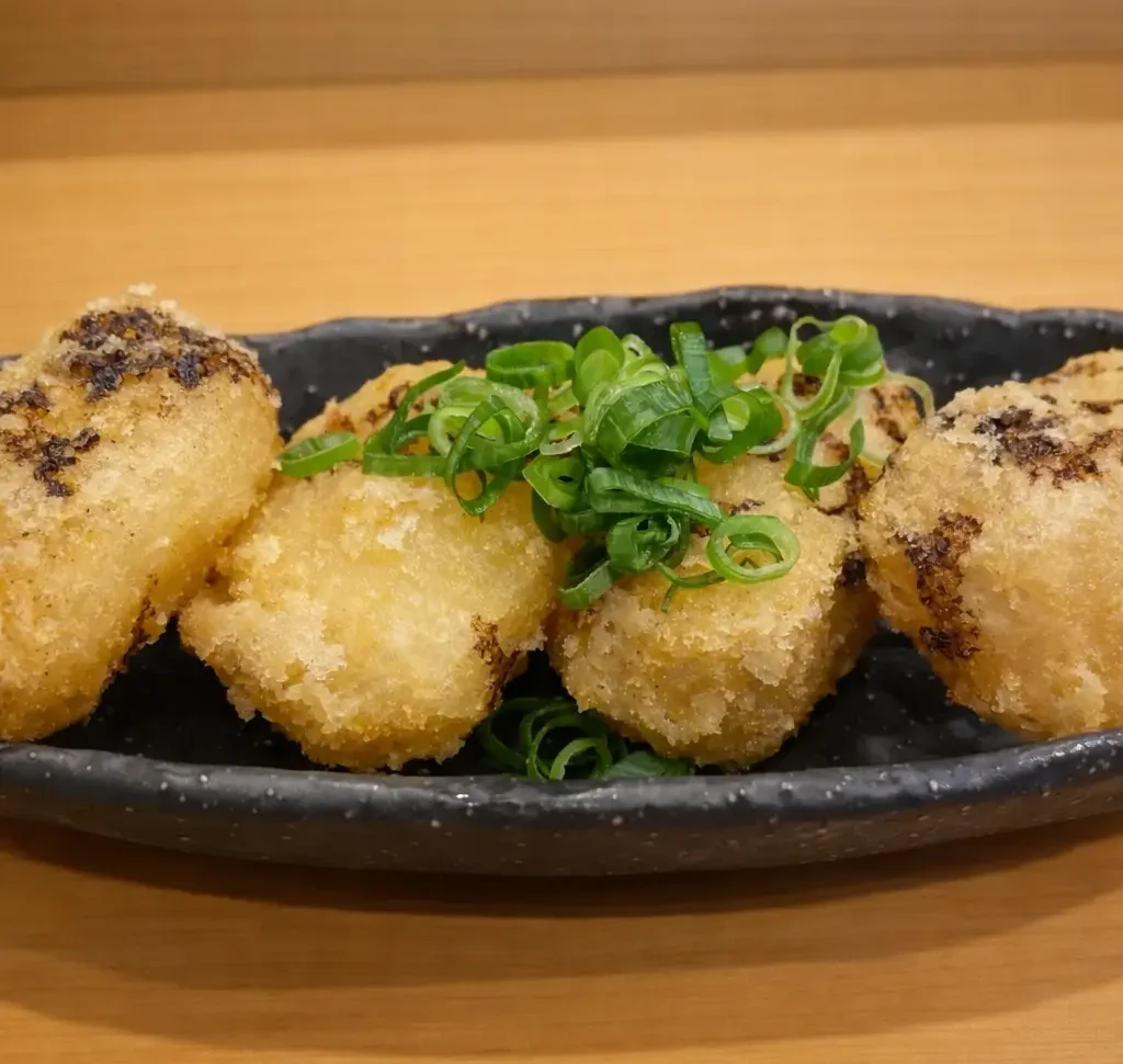 和洋創作居酒屋丸の『おでん大根の唐揚げ』。出汁を含ませた大根を香ばしく揚げ、黒い器に盛り付けて青ねぎを添えた料理写真